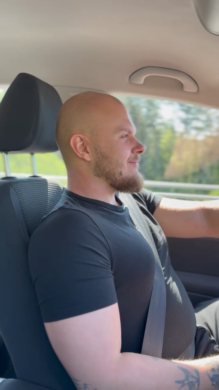Alex kör bil en solig dag med grönska utanför fönstret.