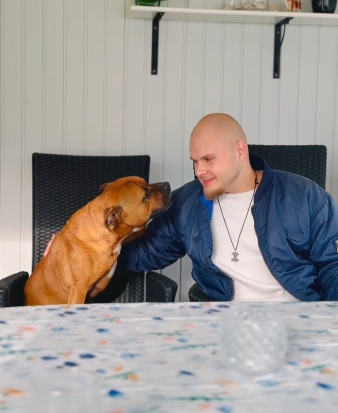 Alex sitter vid ett bord tillsammans med sin hund i en ljus veranda.